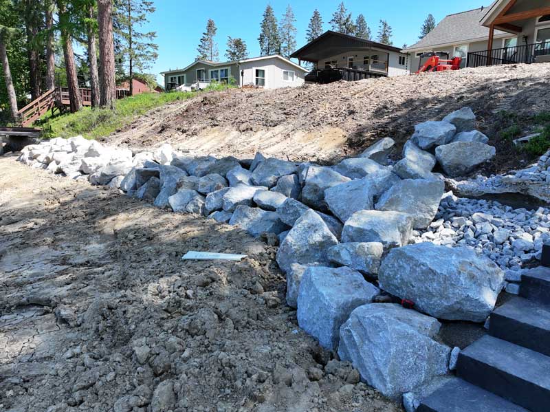 large rocks lined at the bottom of a hill to act as a retaining wall