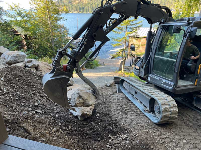 man operating a bulldozer arm to pick up a large rock for a retaining wall