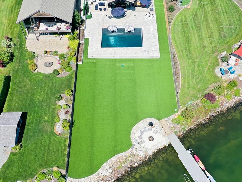 aerial view of a back yard with multiple houses and a green backyard lawn and a river at the bottom