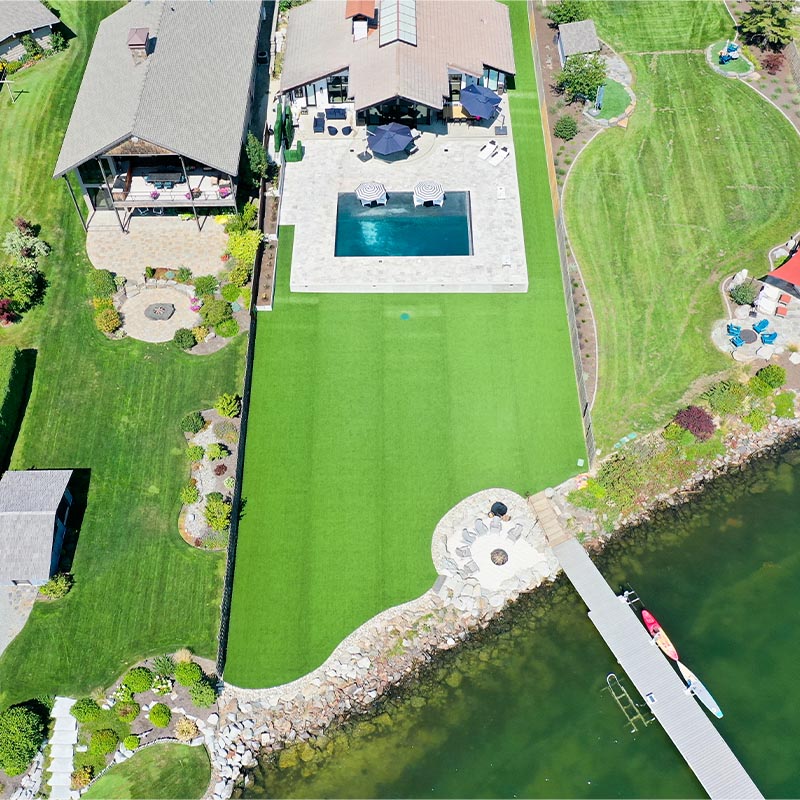 aerial view of a back yard with multiple houses and a green backyard lawn and a river at the bottom